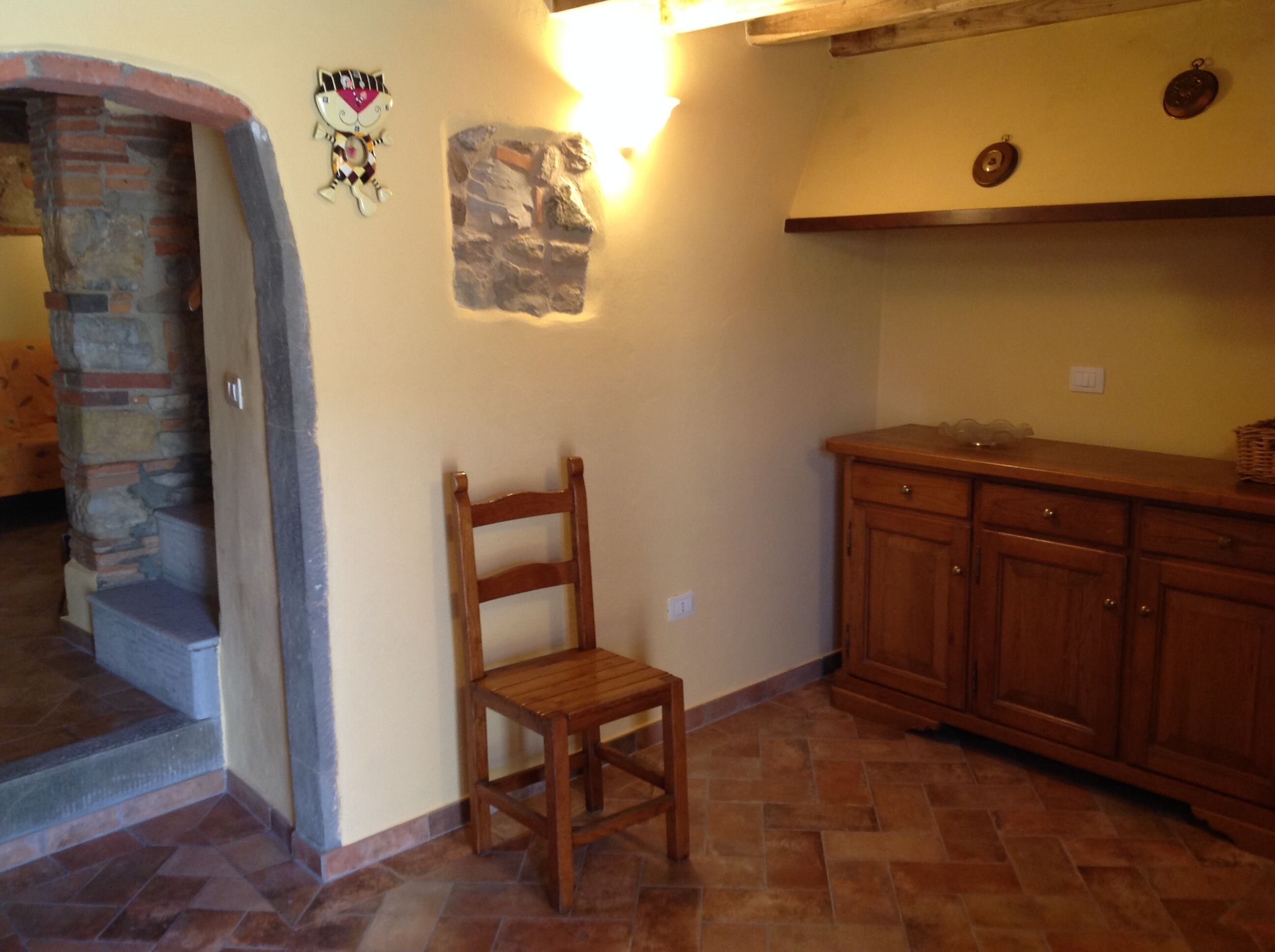 A kitchen with a wooden chair, a stone wall, and a wooden cabinet.