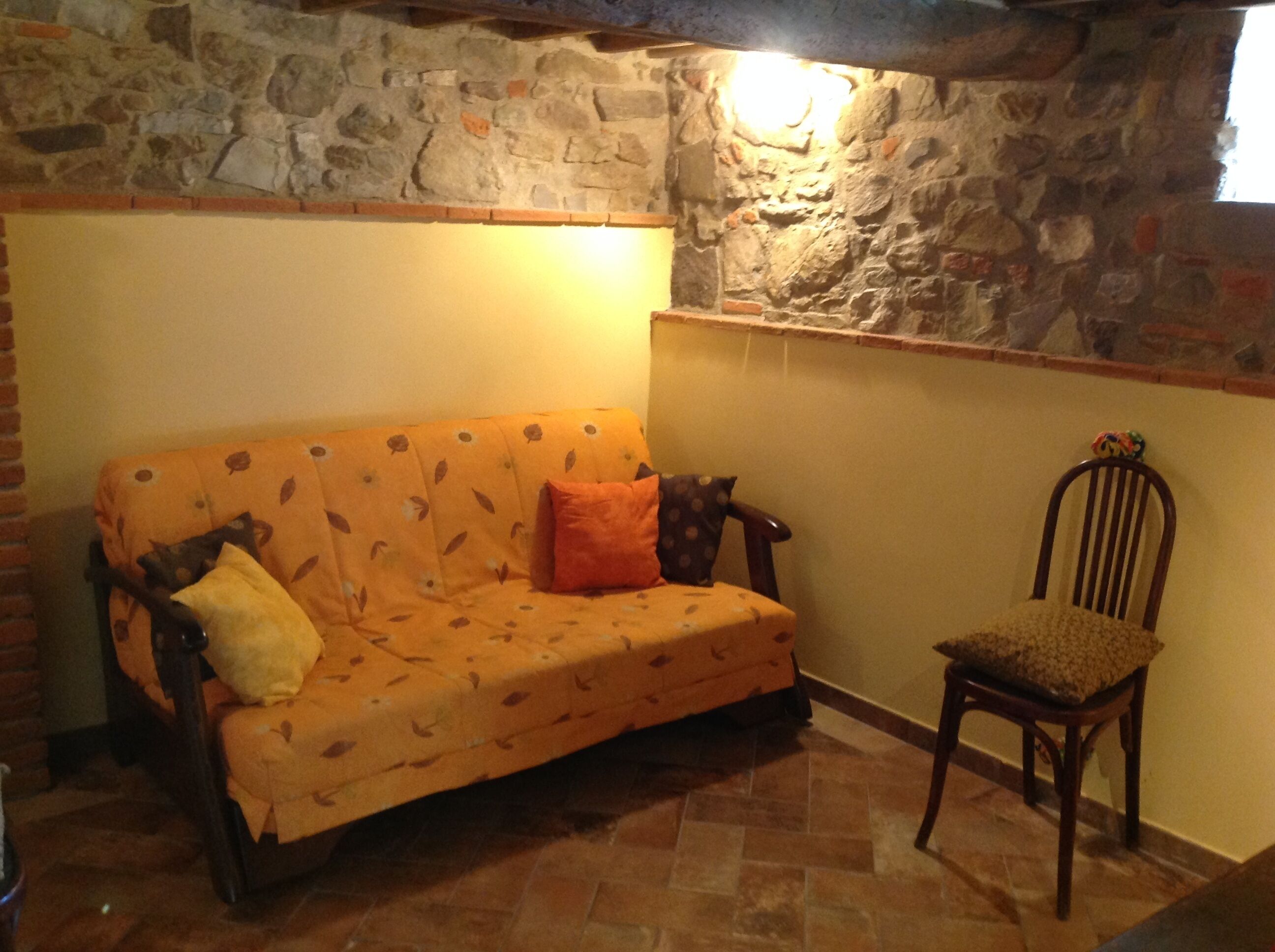 A cozy room with a sofa and a chair, a stone wall, and a window.
