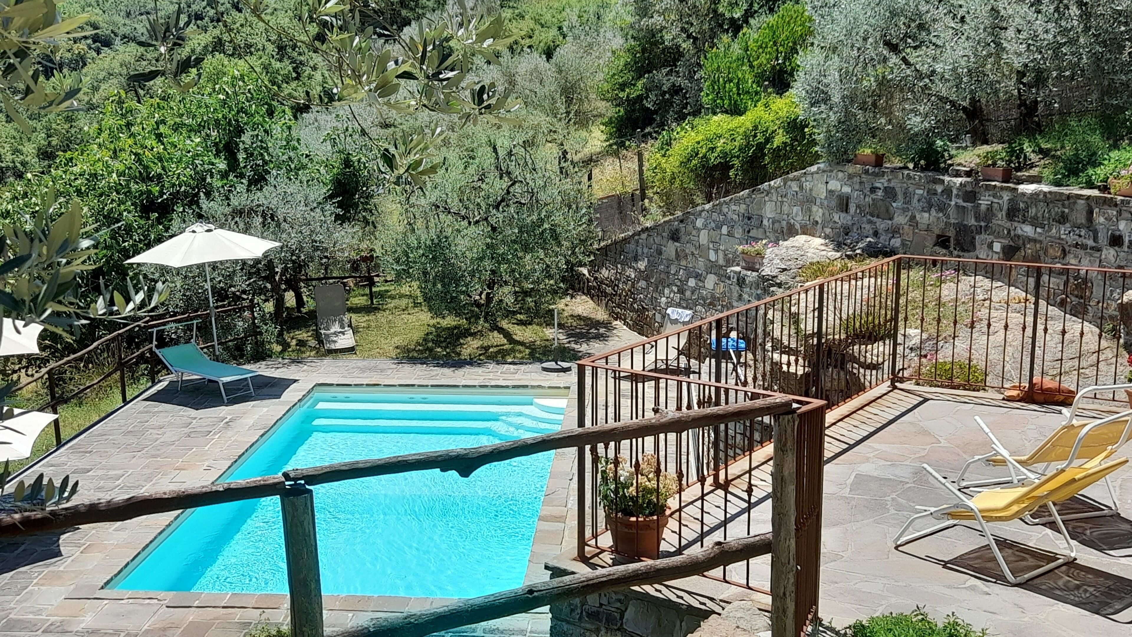 A swimming pool with a stone deck, surrounded by lush greenery and a stone wall.