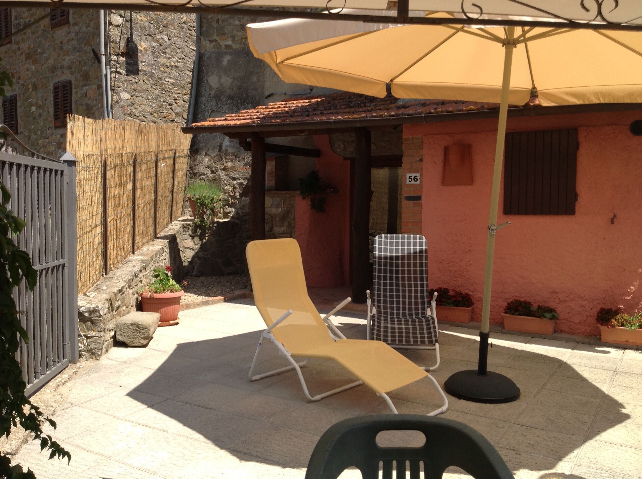 A patio with a yellow lounge chair, a checkered chair, and a large umbrella.