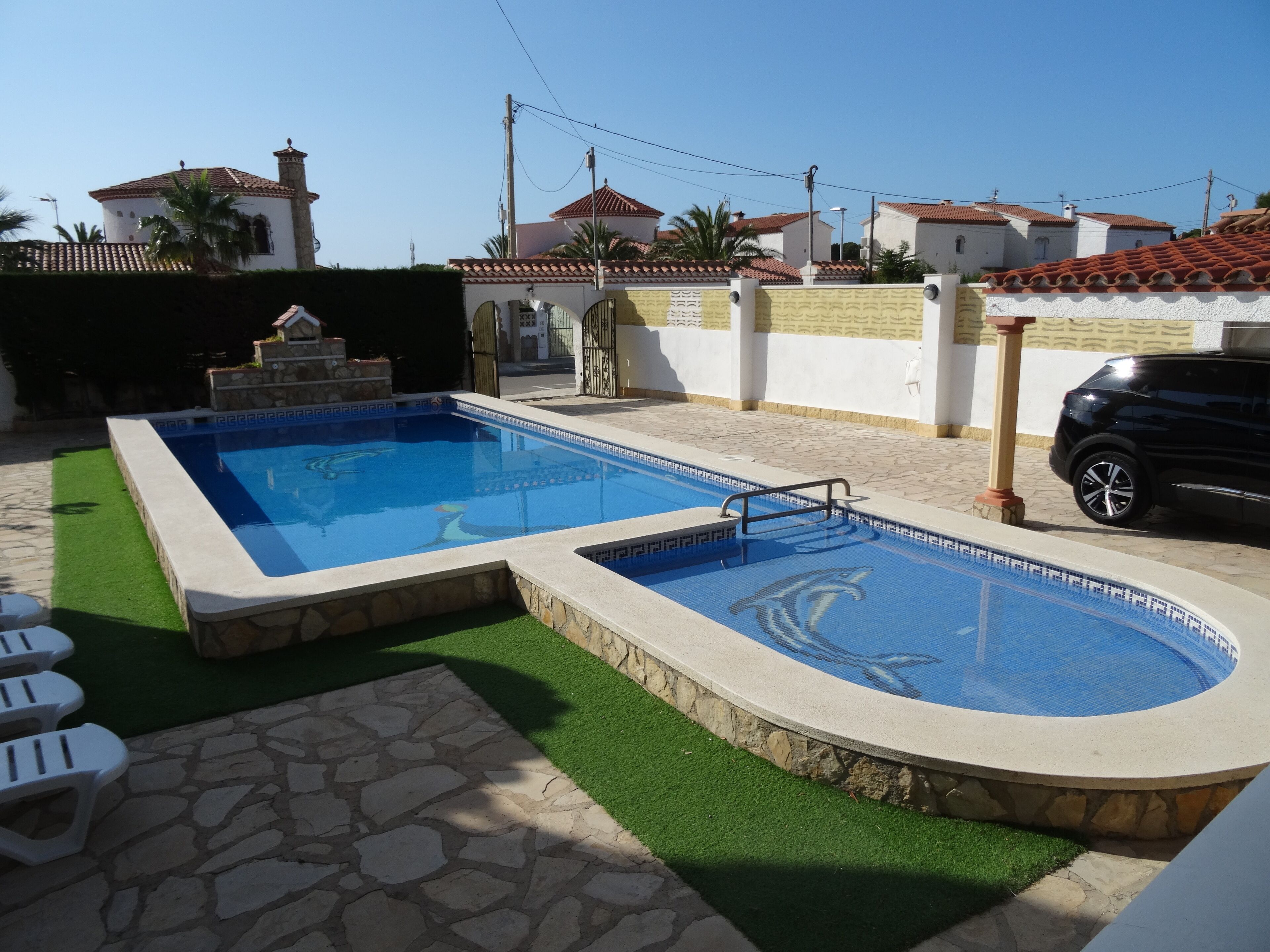 Piscina retangular com borda de pedra e seção circular, ladeada por um terraço de pedra e grama sintética.
