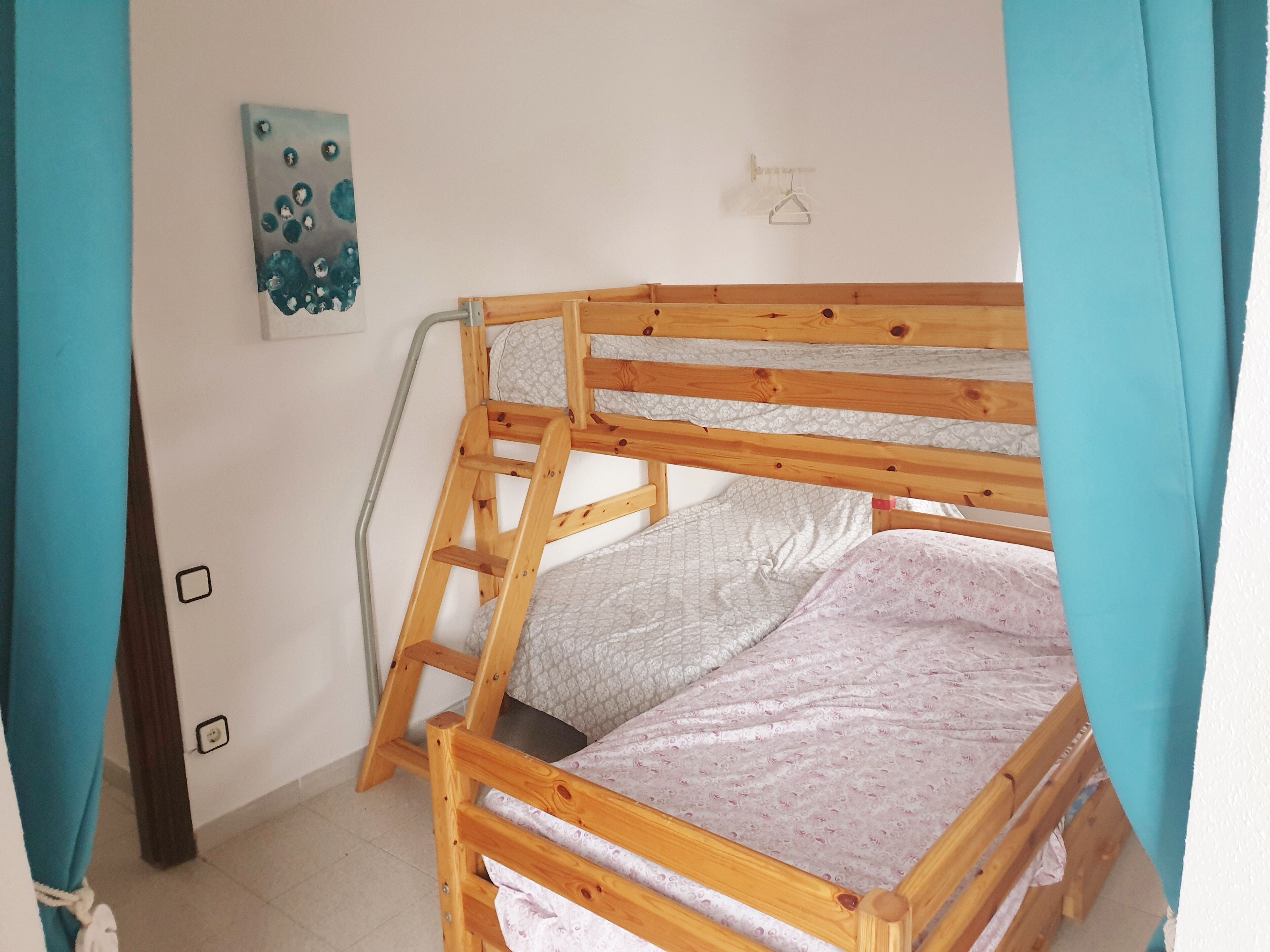 A bunk bed with a ladder, a wall-mounted light switch, and a painting.