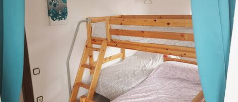 A bunk bed with a ladder, a wall-mounted light switch, and a painting.