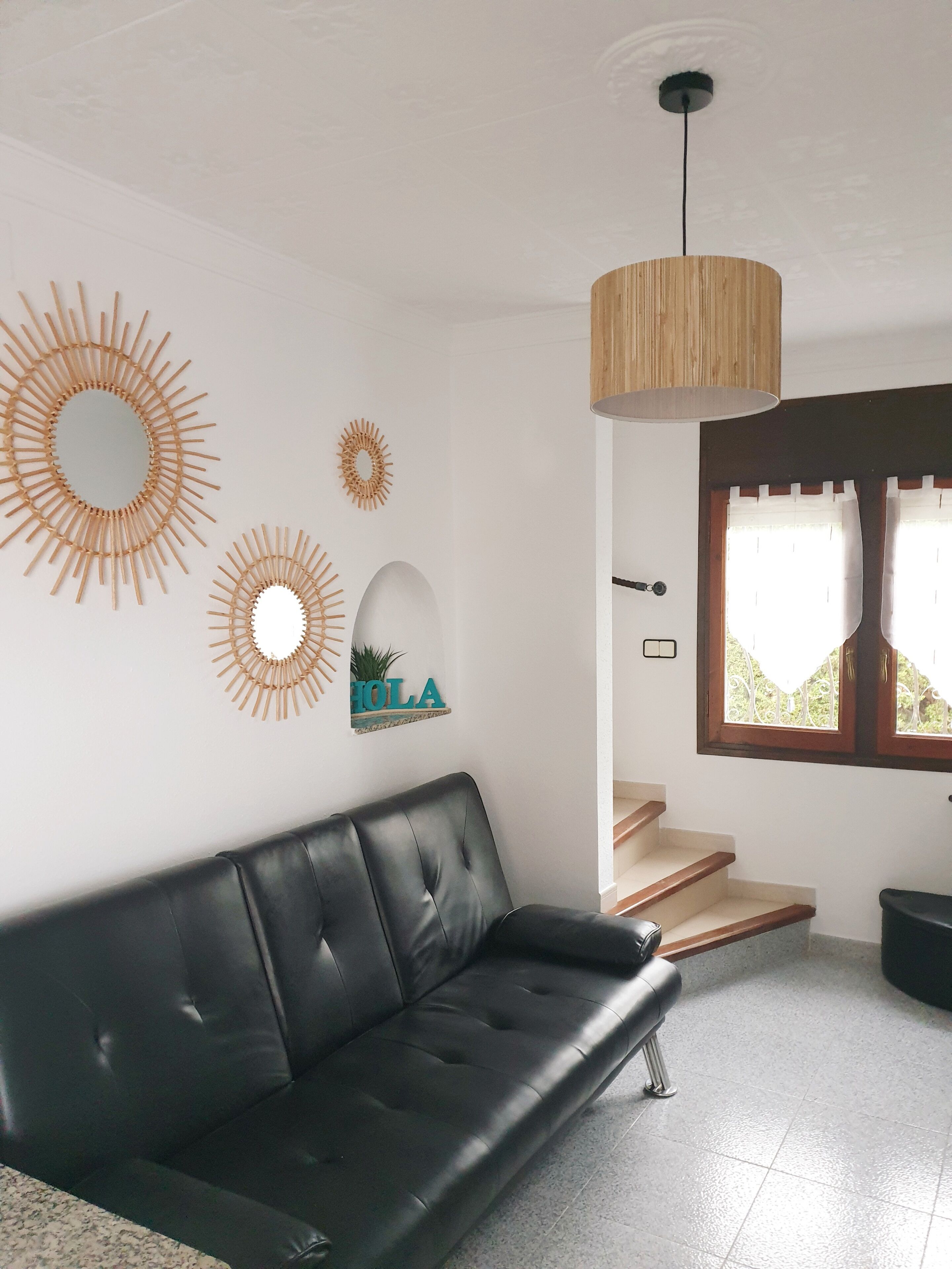 Ein modernes Wohnzimmer mit einem schwarzen Ledersofa, einer Holzzellentrale und Wanddekoration, darunter Sonnenstrahlmuster und ein Schild mit dem Schriftzug "HOLA".