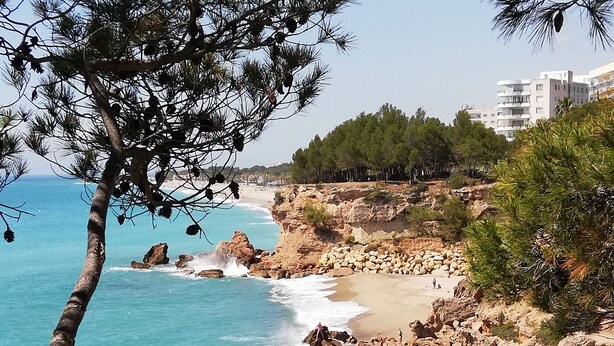 Paesaggio costiero con terreno roccioso, spiaggia sabbiosa e mare cristallino.