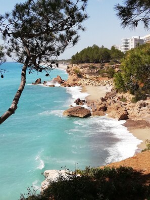 A coastal landscape with rocky terrain, a sandy beach, and a clear blue sea.