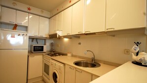 A compact kitchen with white cabinets, a microwave, a sink, and a washing machine. - BEACH APARTMENT 2rooms with PARKING (Tossa de Mar)