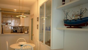 A compact kitchen with white cabinets, a microwave, and a dining area with a white table and chairs. - BEACH APARTMENT 2rooms with PARKING (Tossa de Mar)