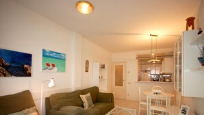 A cozy living room with a sofa and a glass coffee table, a dining area with a table and chairs, and a kitchen visible through an open door. - BEACH APARTMENT 2rooms with PARKING (Tossa de Mar)
