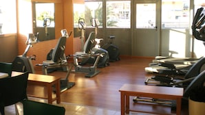 Une salle de sport équipée de matériel d’exercice, dotée de grandes fenêtres et offrant une vue sur la ville.