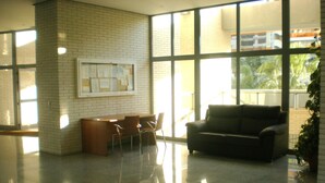 Un hall d’entrée spacieux avec un mur en briques, une cloison en verre, un bureau en bois avec des chaises, un canapé et une plante en pot.