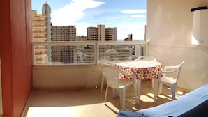 Un balcon avec une table et des chaises, une vue sur les bâtiments de la ville et un ciel dégagé.