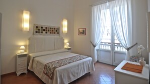 A bedroom with a bed, bedside lamps, a window with curtains, and a small table with a vase. - Stylish Apartment - Minori (Minori)