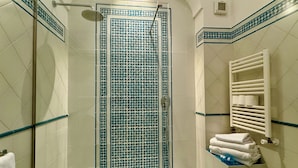 A bathroom with a glass-enclosed shower, a white sink with a towel rack, and a tiled wall with a blue border. - Stylish Apartment - Minori (Minori)