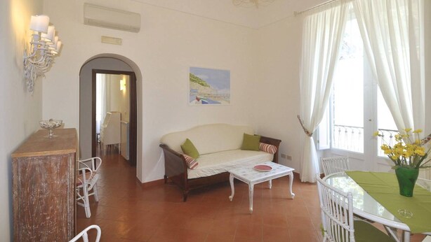 A living room with a sofa, a dining table with chairs, a chandelier, and a painting on the wall. - Stylish Apartment - Minori (Minori)