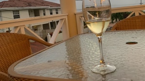 Un bicchiere di vino bianco su un tavolino di vetro, con sedie in vimini, con vista su un edificio con tetto rosso.
