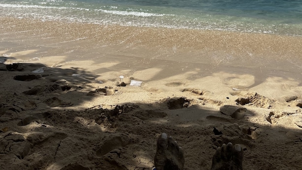 Una spiaggia con acqua cristallina dai riflessi turchini, una riva sabbiosa e un cielo parzialmente nuvoloso.