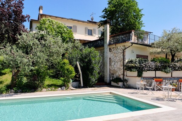 A pool area with a stone wall, outdoor furniture, and a building in the background.
