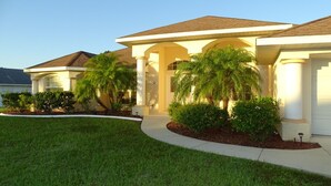 A two-story house with a covered porch, palm trees, and a well-maintained lawn.