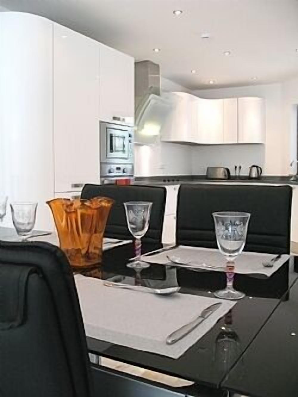 A modern dining area with a black table, white placemats, and clear glasses.