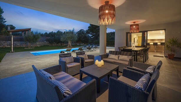 Un patio al aire libre con mobiliario de mimbre, una piscina y una zona de cocina.