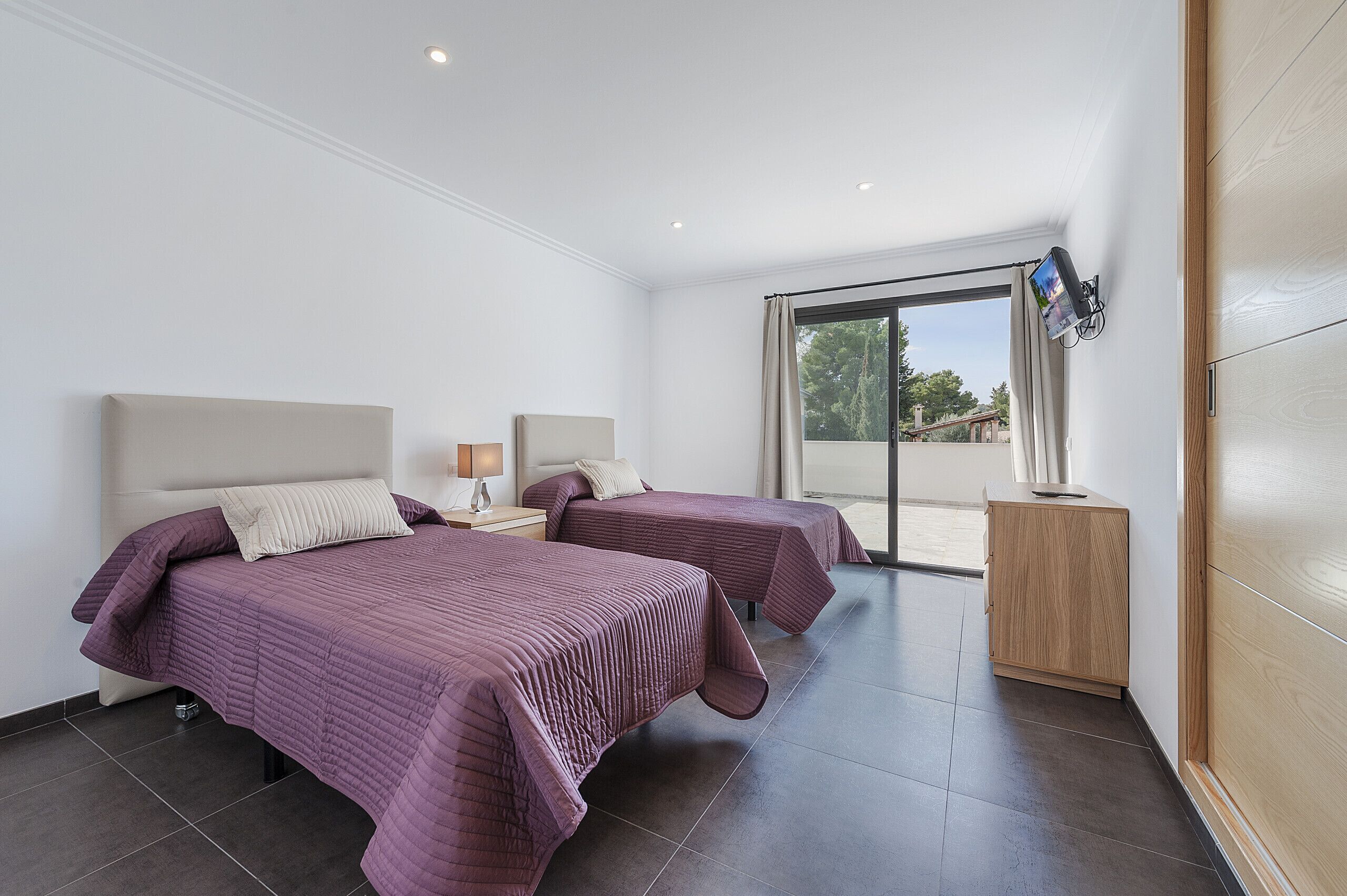 A hotel room with two beds, a TV, and a sliding glass door to the outside.