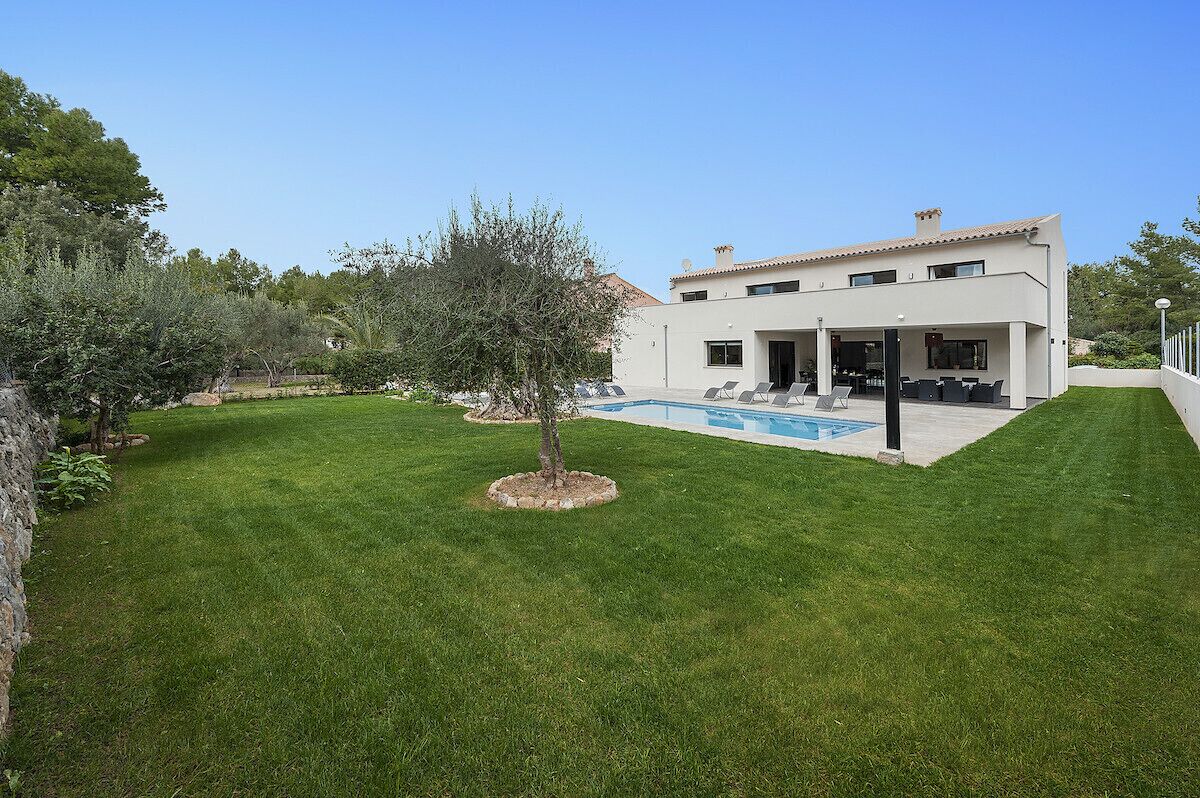 Une maison moderne avec une piscine, entourée d’une pelouse bien entretenue et d’arbres.