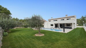 Una casa moderna con piscina, rodeada de un césped cuidado y árboles.