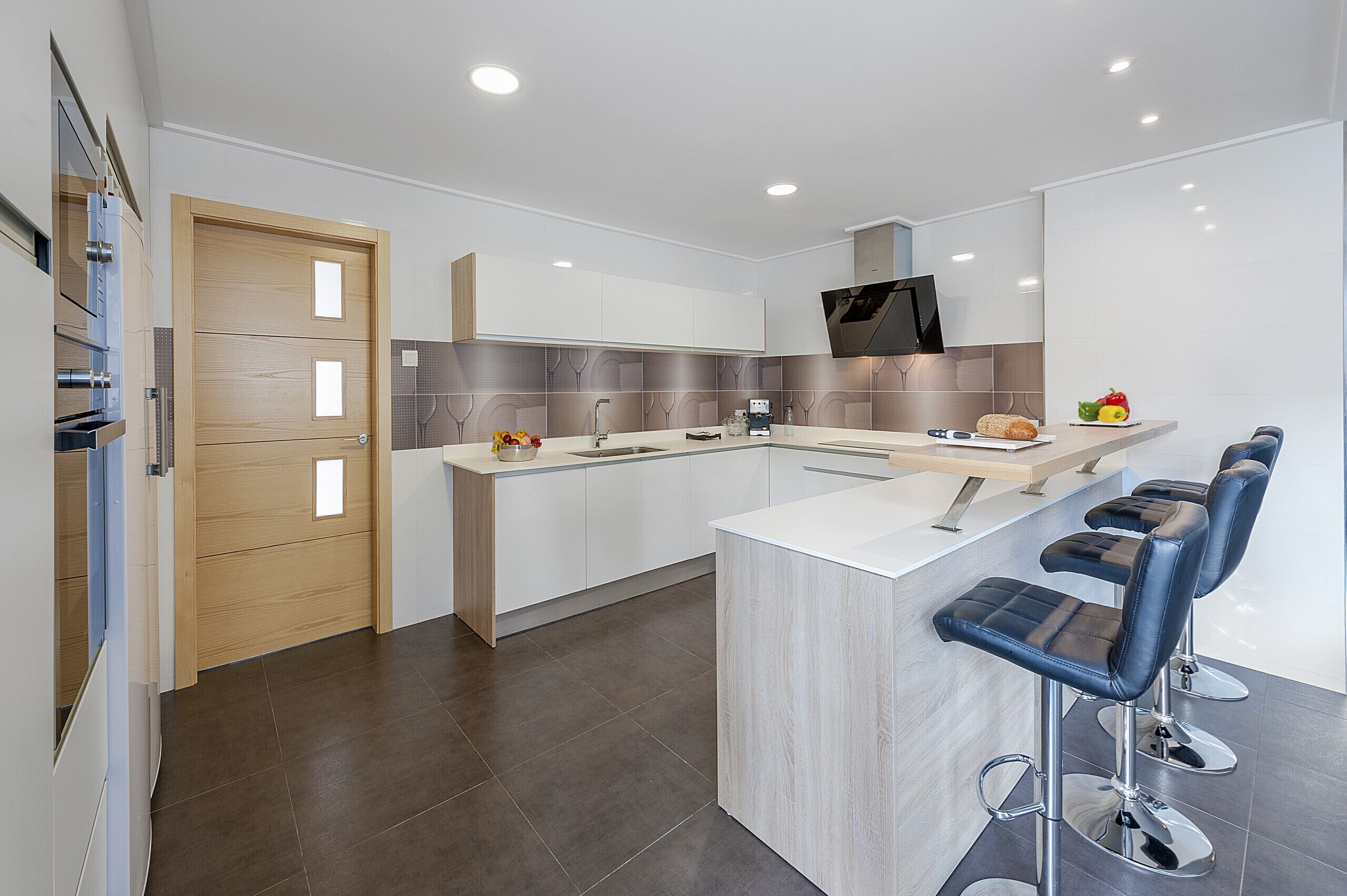 A modern kitchen with a central island, bar stools, and a flat-screen TV.