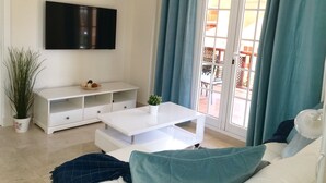 A living room with a flat-screen TV, a white coffee table, and a sofa with teal cushions. - Monte Carrera The Little Mermaid (Arguineguin)