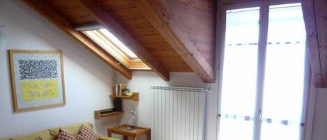 A cozy room with a wooden ceiling, a sofa with checkered cushions, a small table, and a window with blinds.