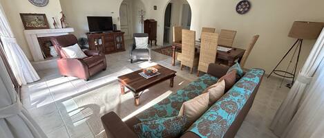 A spacious living room with a sofa, armchairs, a coffee table, and a dining area with chairs and a table.