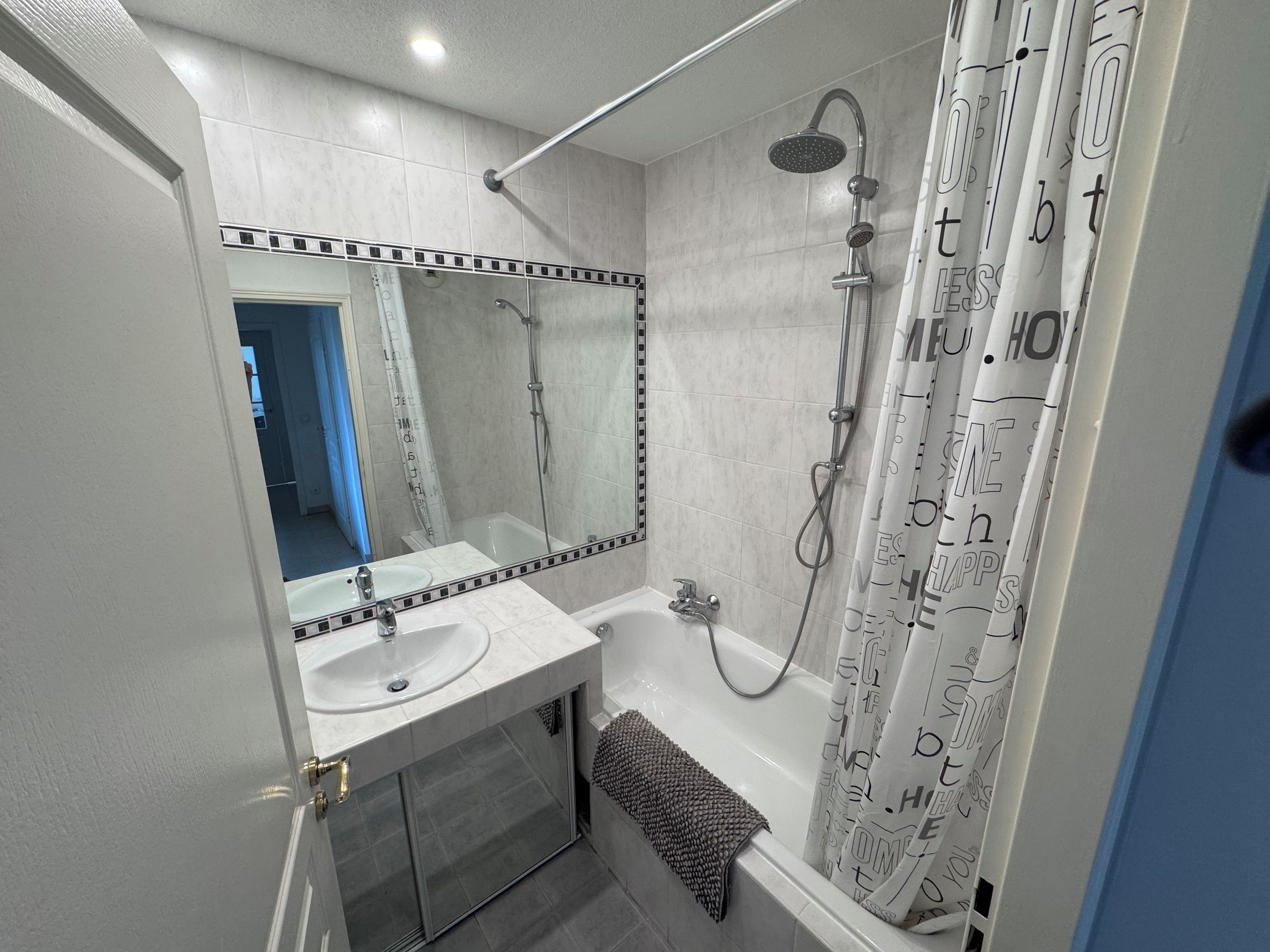 Een badkamer met een bad, douche, wastafel en spiegel.