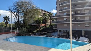A swimming pool with lounge chairs, a building with balconies, and a palm tree.