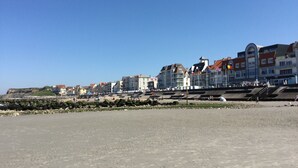 Une ville côtière avec des bâtiments qui bordent la plage, un littoral rocheux et un ciel bleu dégagé.