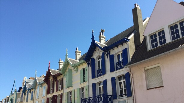 Une rangée de bâtiments aux couleurs vives, chacun présentant un style architectural distinct, notamment des bow-windows et des balcons décoratifs.