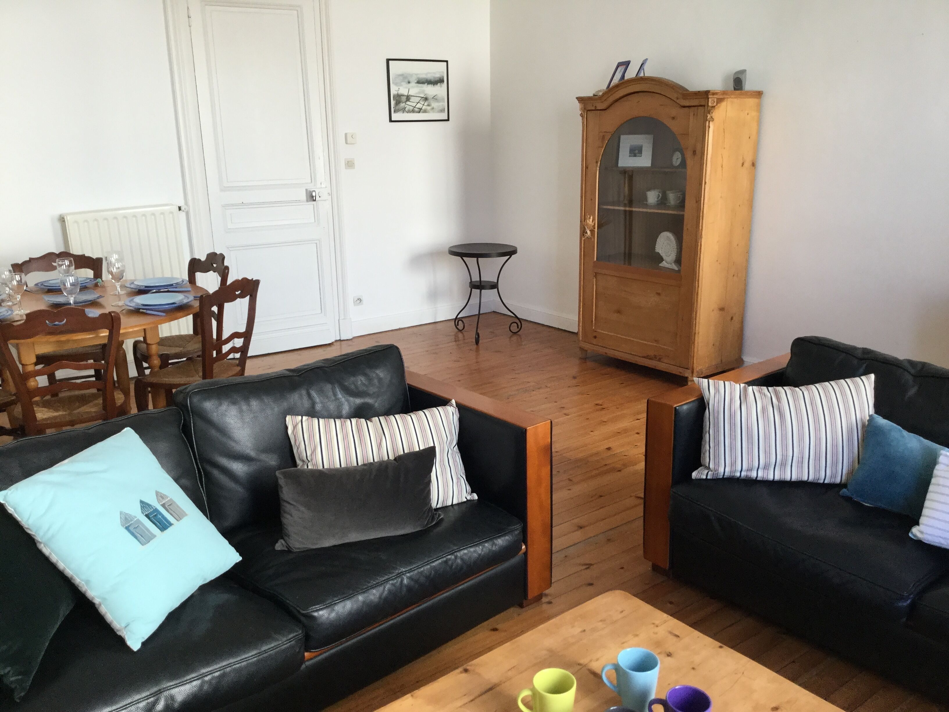 Una sala de estar con dos sofás de cuero negro, una mesa de centro de madera y un comedor con una mesa y sillas de madera.