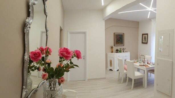 A room with a large mirror, a vase with pink flowers, a white table with chairs, and a white cabinet. - Fantastic Penthouse in the center of Rome not far from the Vatican (Roma)