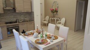 A dining area with a table set for four, surrounded by white chairs. A kitchen with modern appliances and a tiled backsplash is visible in the background. - Fantastic Penthouse in the center of Rome not far from the Vatican (Roma)