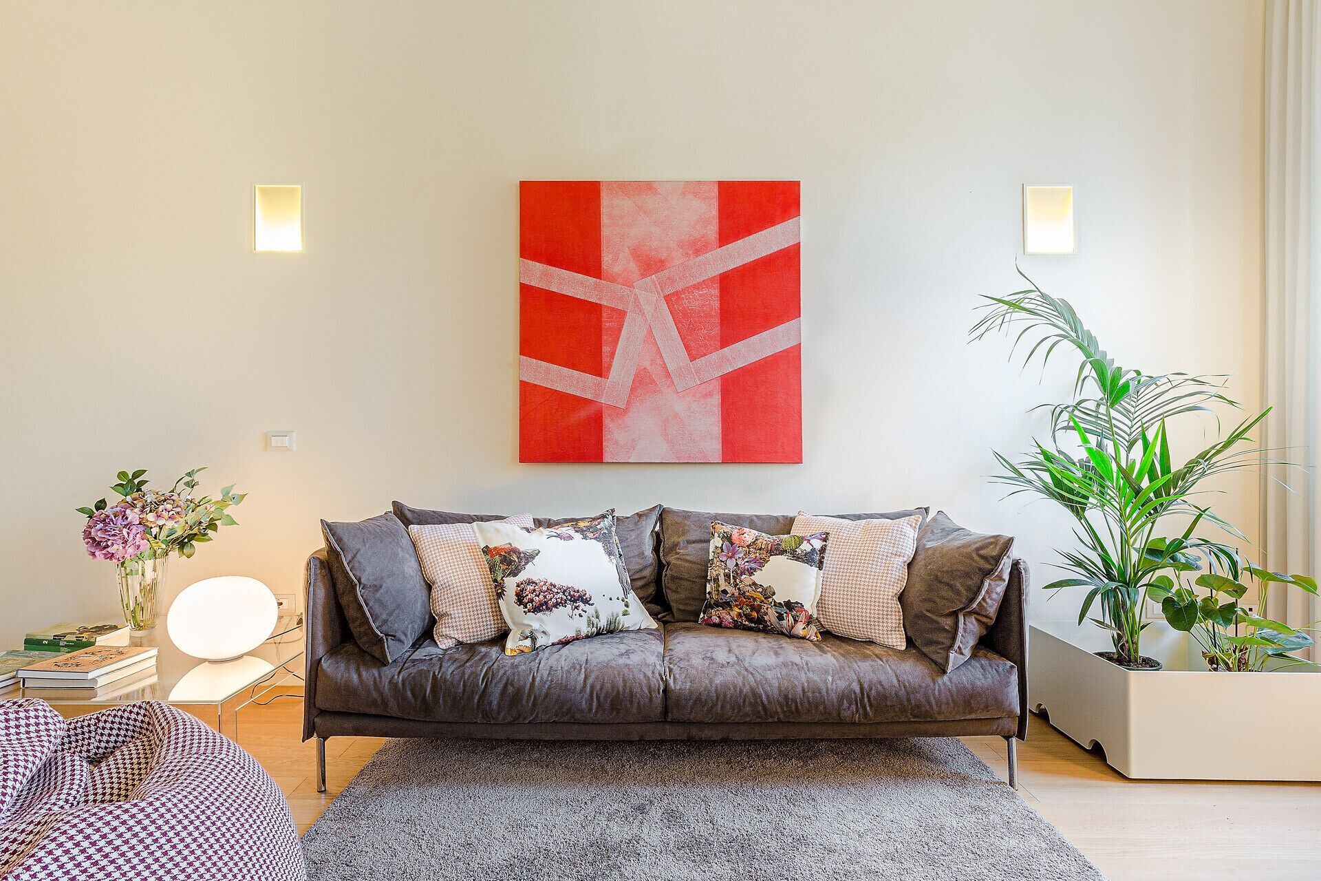 Una sala de estar moderna con un sofá gris, un cuadro abstracto rojo y una planta en maceta.