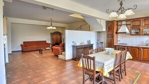 Ein großzügiger Wohnbereich mit einer Couch, einem Esstisch mit Stühlen, einer Küche mit Holzschränken und einer Treppe, die ein weiteres Stockwerk hinaufführt.