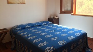Quarto com cama coberta por um edredom azul com estampas de peixes, uma pequena mesa de cabeceira com abajur e duas obras de arte nas paredes.