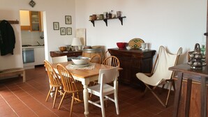 Uma área de refeições com mesa e cadeiras de madeira, cozinha ao fundo e um lustre.
