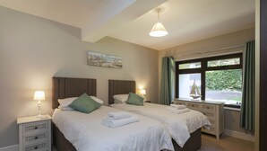 A double room with two beds, bedside tables, lamps, a painting, and a window with curtains. - Burnham A -  a self catering cottage that sleeps 3 guests  in 1 bedroom (Holt)