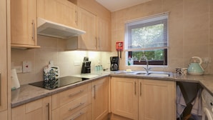 A modern kitchen with wooden cabinets, a built-in stove, and a window with blinds. - Burnham A -  a self catering cottage that sleeps 3 guests  in 1 bedroom (Holt)
