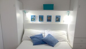 A bed with white bedding and two blue pillows, a white headboard, and four framed pictures on the wall above. - Charming and cozy little house in the center of Pomonte, just steps from the sea (Pomonte)