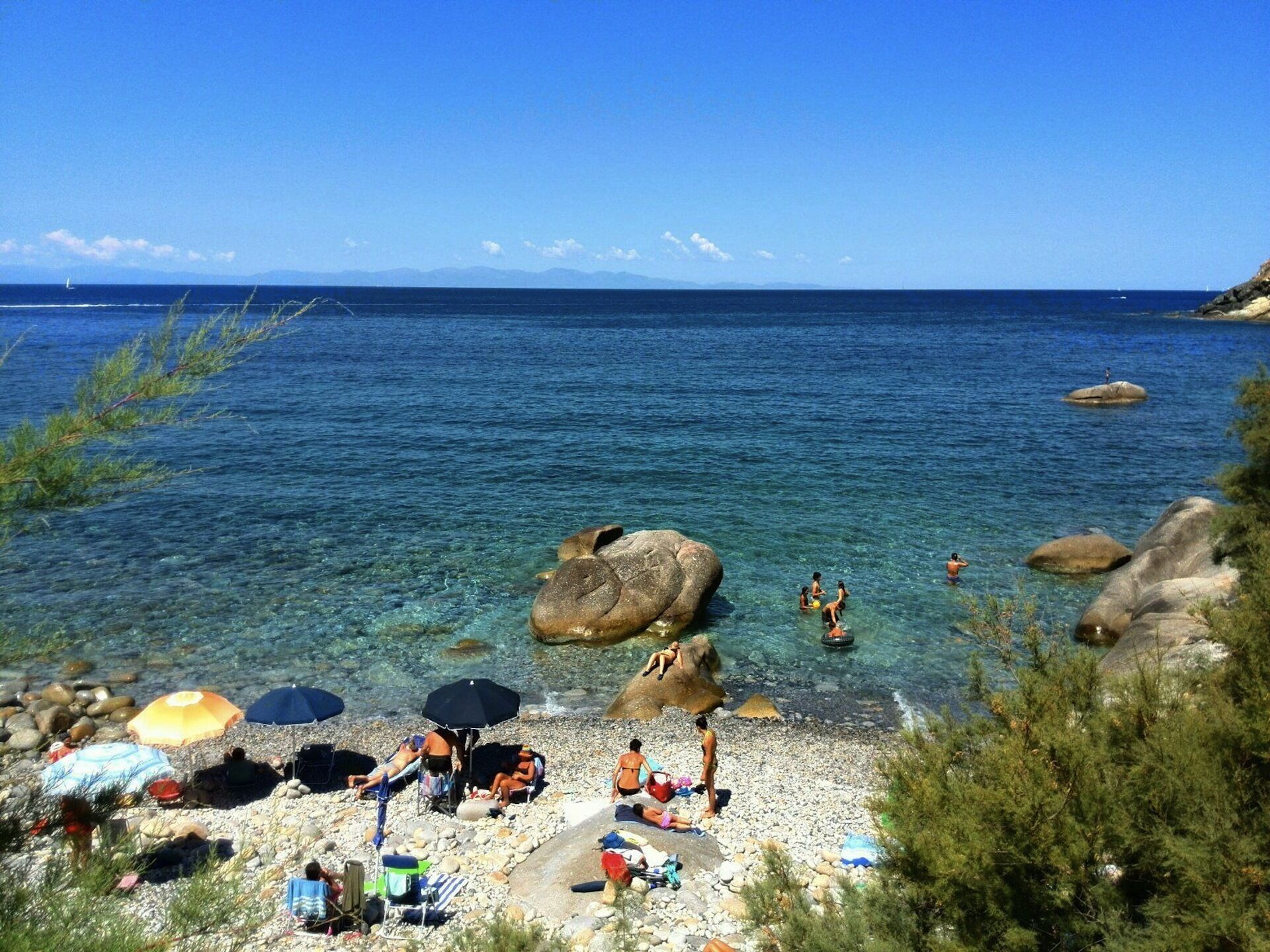 Une plage avec une eau claire, des rochers et des gens qui prennent un bain de soleil.