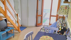 A room with a dining table, chairs, a laptop on a blue cart, a wardrobe, and a door leading outside. - Charming and cozy little house in the center of Pomonte, just steps from the sea (Pomonte)