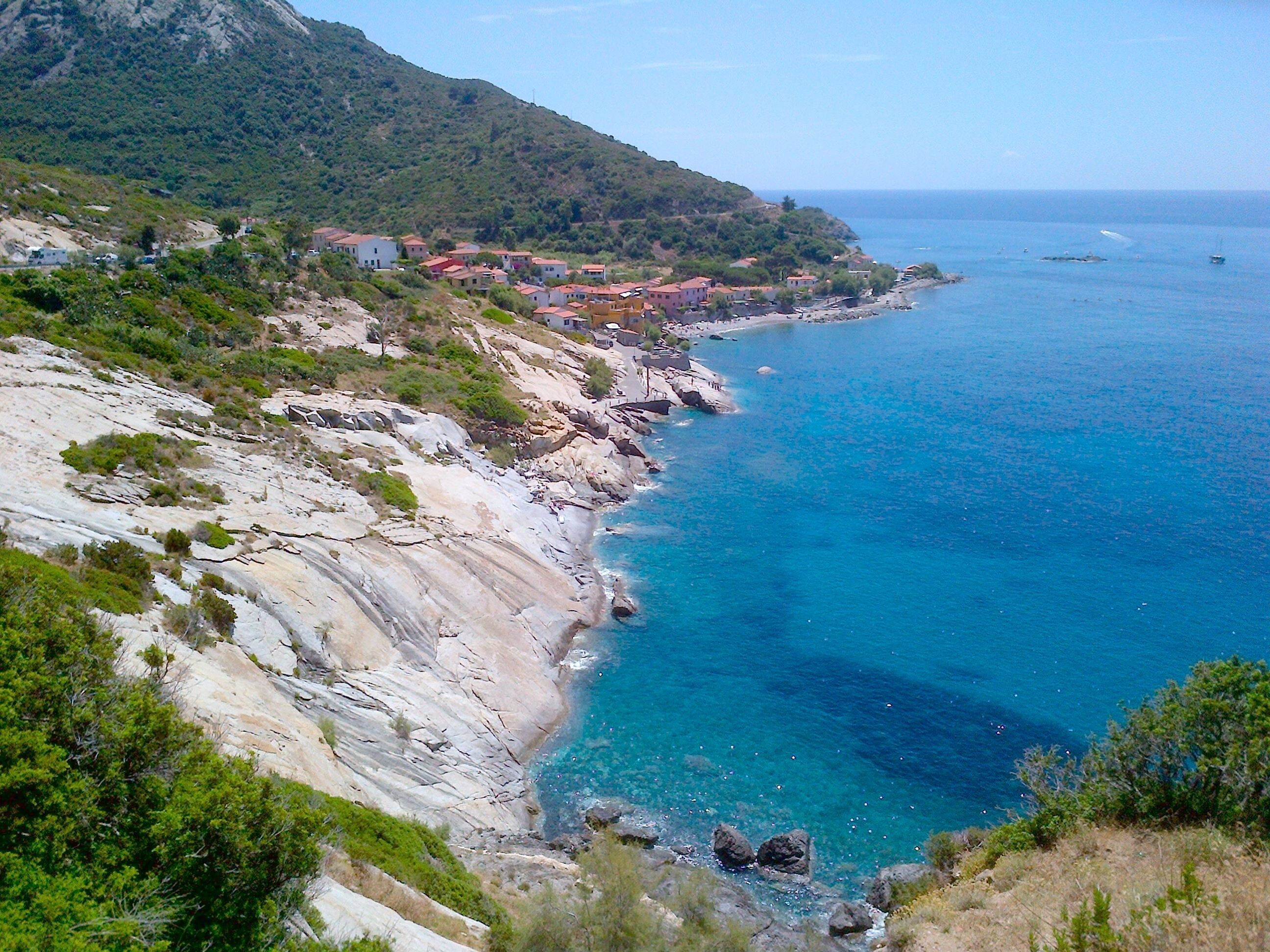 Eine Küstenstadt mit schroffen Klippen, blauem Meer und Häusern mit roten Dächern.