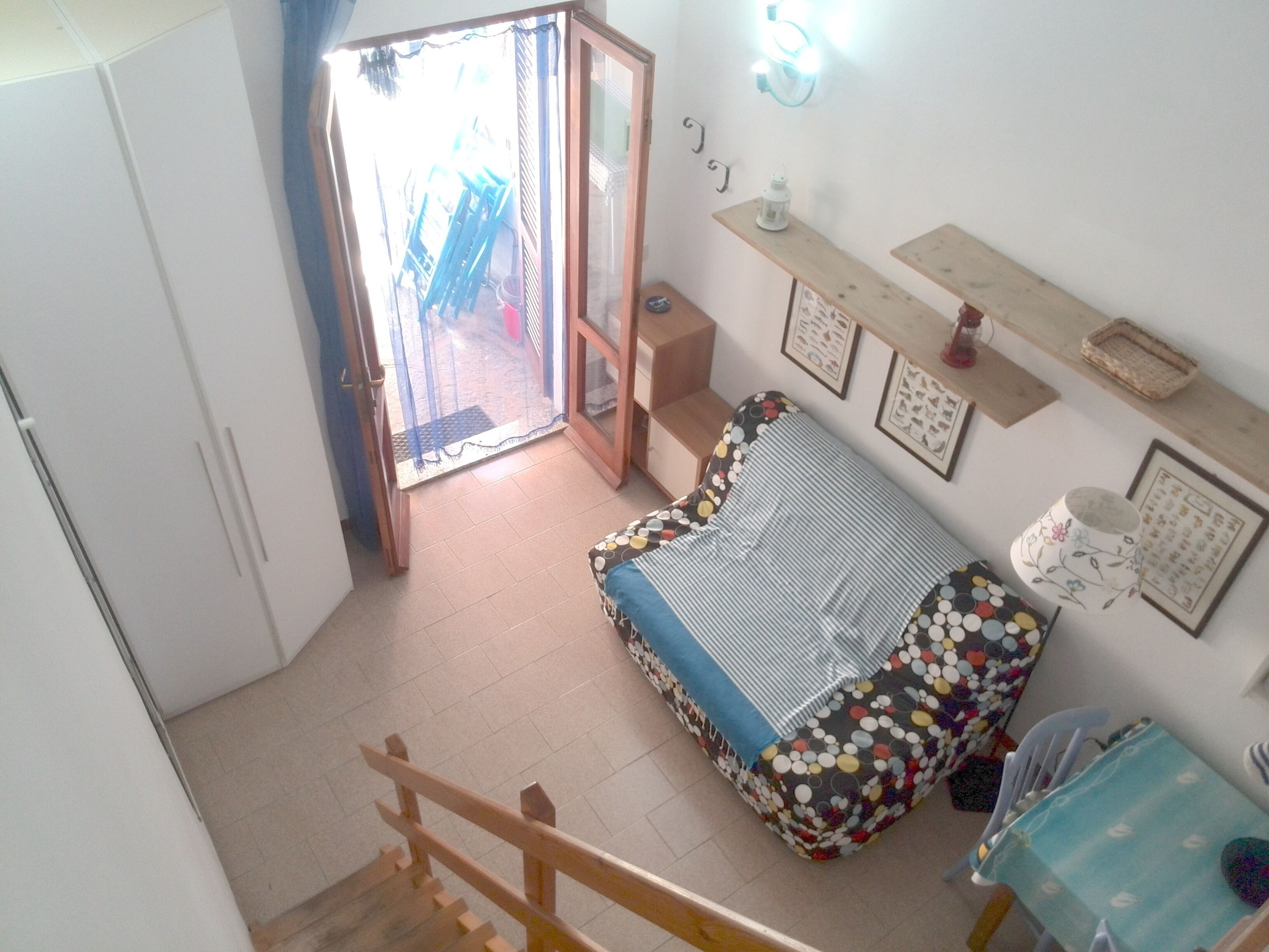 A bedroom with a bed, a small table, and a chair. There is a door leading to a balcony.